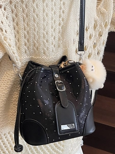 Minimalist black bucket bag in shiny patent leather with silver rivets and plush charm