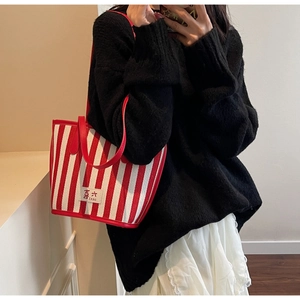 Red and white striped tote bag with leather patch held by model in casual outfit