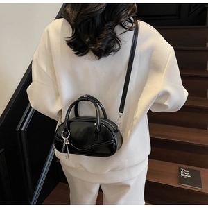 Detail of glossy black bowling bag with silver key charm on white casual outfit