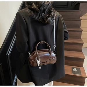 Detail of dark brown polished bowling bag with vintage key charm on indoor wooden stairs