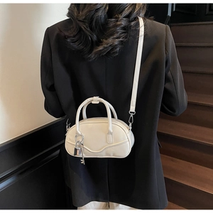 Detail of a creamy white PU leather bowling handbag with silver lock charm on a model