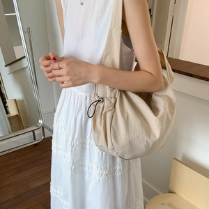 Detail view of the beige dumpling bag with adjustable black drawstring and toggle