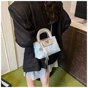 Quilted blue crossbody bag with heart buckle and lace detail on female model's shoulder