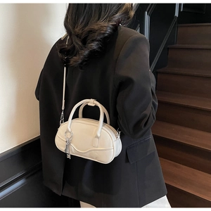 Close-up of cream bowling bag with metal key charm and slender detachable shoulder strap