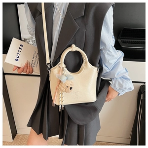 Detail einer beigen Beuteltasche mit Lychee-Struktur und blauem Bärenanhänger