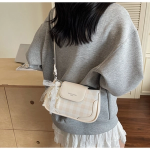 Details einer beigen karierten Handtasche mit Spitzenschleife und Perlenanhänger am Gurt