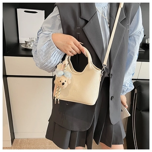 Detail of cream bucket bag showing pebble leather texture and cute bear charm with bow