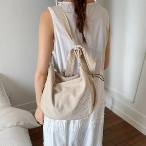 Detail view of large beige dumpling bag with knotted shoulder strap and pleated texture