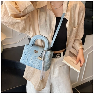 Close-up of light blue quilted handbag with heart buckle and lace bear charm detail