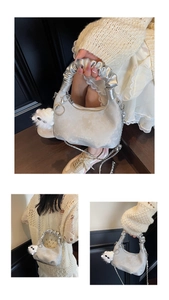 Detail of silver metallic crescent bag featuring pleated handle and plush ball charm