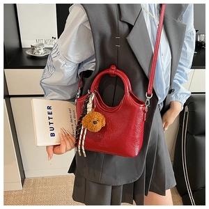 Close-up of bright red patent leather bucket bag with cute brown teddy bear charm