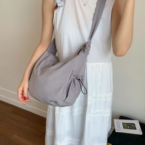 Detail of the grey nylon dumpling bag featuring a wide knotted shoulder strap on a model