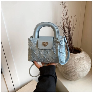 Close-up of light blue denim textured crossbody bag with silver heart-shaped metal lock