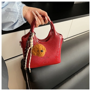 Close-up of red pleated bucket bag with plush puppy charm and braided cord details