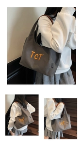 Macro shot of grey canvas tote bag with orange TCT embroidery and brown leather shoulder strap