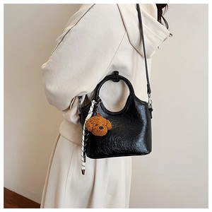 Detail of black pleated bucket bag with teddy bear charm and striped ribbon decoration