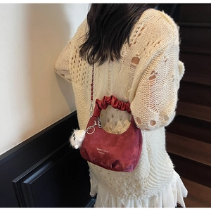 Detail of dark red cloud bag with pleated handle and plush charm on a knit sweater
