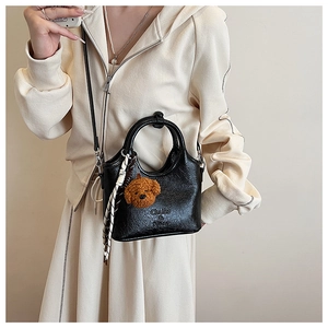 Detail of black pebbled leather bucket bag featuring a bear charm and striped silk scarf