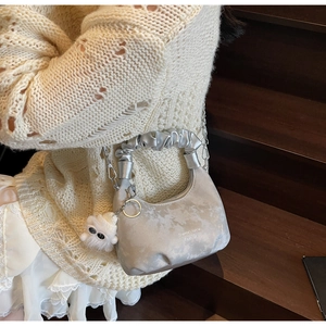 Close-up of a silver cloud bag with ruched handles, metal chain, and cute plush charm