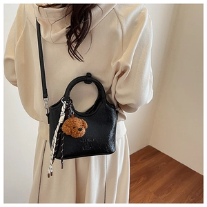 Detail of black leather bucket bag featuring a teddy bear charm and woven tassel accent