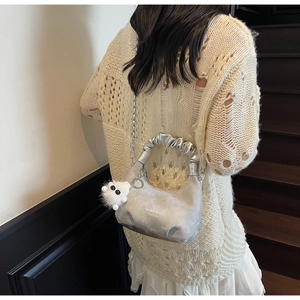 Silver crescent shoulder bag with pleat detail and plush charm on beige knit sweater