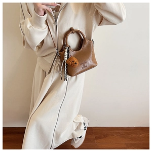 Detail of a brown leather bucket bag with dog plush charm and striped ribbon handle