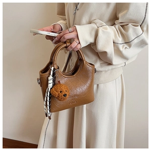 Close-up of brown textured leather bucket bag with plush poodle charm and braided rope detail