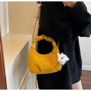 Detail of yellow pleated cloud bag with gold chain strap and plush pendant accessory