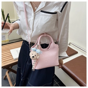 Pink lychee grain bucket bag with teddy bear charm shown in a minimalist outdoor cafe setting