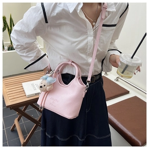 Detail of light pink pebble leather bucket bag with plush bear charm and long strap