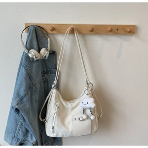 Close-up of a white tote bag featuring metal buckle pocket and cloud plush charm