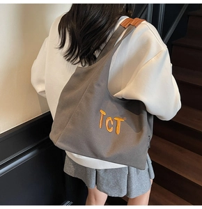 Vue de côté du sac cabas en toile gris foncé avec broderie orange sur tenue décontractée