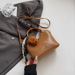 Detail of brown leather bucket bag with plush bear charm and checkered scarf on grey blazer