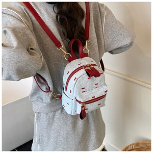 Détail d'un mini sac à dos tissé blanc avec broderies de nœuds rouges et métal doré