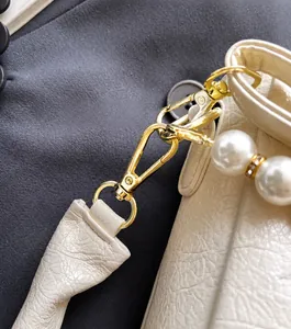 Detaillierte Makroansicht der cremeweißen Lederstruktur mit Perlenkette und goldenen Beschlägen