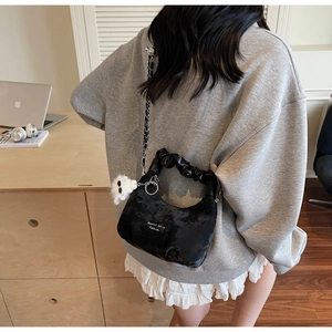 Detail of black velvet crescent bag with pleated handle, silver chain, and plush charm