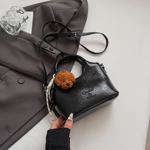 Detail of black textured leather bucket bag with teddy bear charm on grey suit background