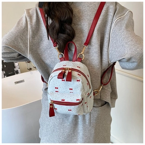 Vue arrière d'un mini sac à dos tissé blanc à nœuds rouges porté par un mannequin