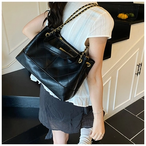 Detail of black quilted tote bag with gold chain strap and glossy leather finish