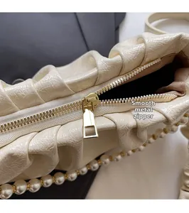 Detailansicht des goldenen Reißverschlusses und der Perlenkette an der cremefarbenen Tasche