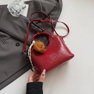 Detailed view of red textured leather bucket bag with plush bear charm on grey blazer