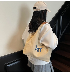Détail des lettres brodées bleues et de l'anse en cuir sur un sac fourre-tout beige
