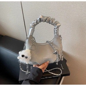Silver-grey crescent bag with wrinkled cloud handle and white plush charm on a book