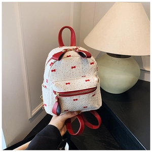 Détail du mini sac à dos blanc avec nœuds rouges et texture en cuir synthétique