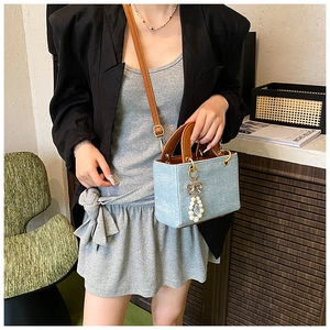 Detail of light blue denim mini square bag with brown handle and pearl bow charm