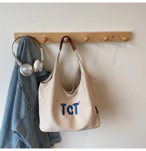Détail d'un sac cabas en toile crème avec broderie TCT bleue et poignées en cuir brun