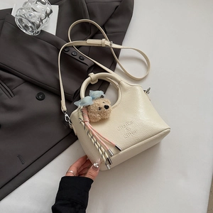 Detail of cream-colored leather tote bag featuring a plush bear charm and brand logo