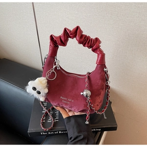 Close-up of burgundy suede dumpling bag featuring a ruched handle and plush monster charm
