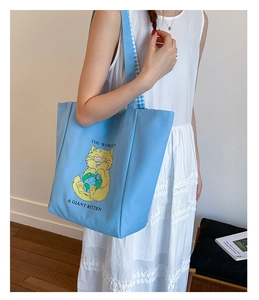 Detail of light blue canvas tote bag with cartoon cat print and blue plaid strap lining