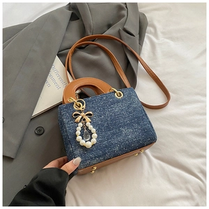 Detail of blue denim shoulder bag featuring brown leather strap and pearl bow charm